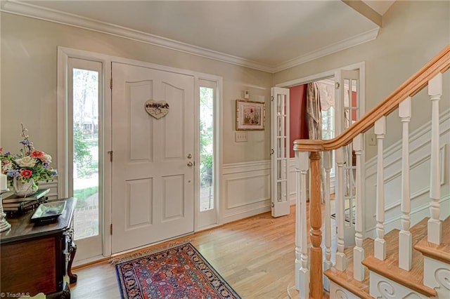 entrance foyer with crown molding, light wood-style flooring, stairway, and a decorative wall