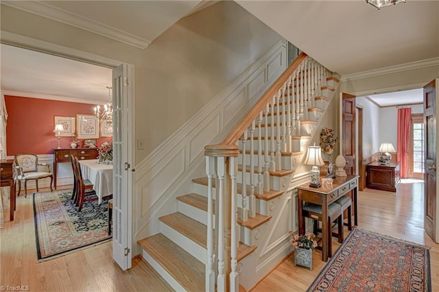 stairway featuring ornamental molding, a decorative wall, wood finished floors, a wainscoted wall, and a chandelier