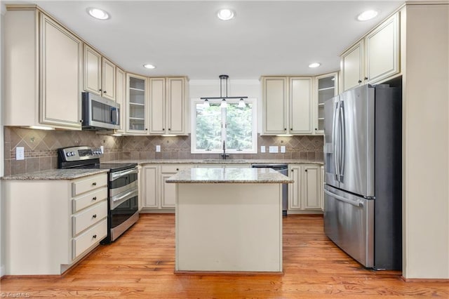 kitchen with a sink, stainless steel appliances, glass insert cabinets, light wood-type flooring, and a center island