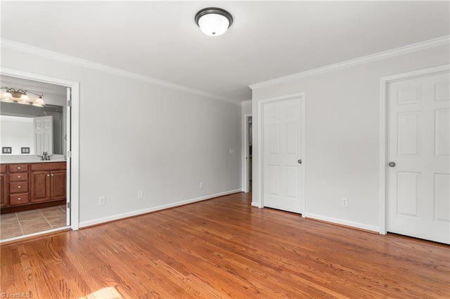 unfurnished bedroom with ensuite bath, ornamental molding, light wood finished floors, a sink, and baseboards