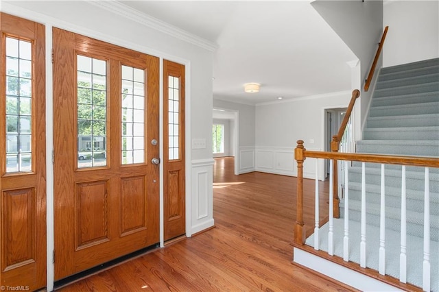 entrance foyer with wood finished floors, stairs, a decorative wall, ornamental molding, and a wainscoted wall