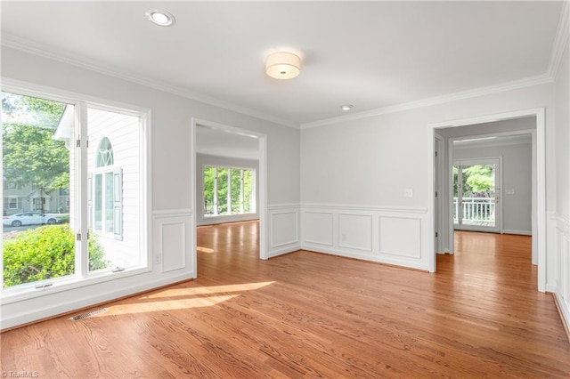 empty room with wainscoting, light wood-style flooring, crown molding, and a decorative wall