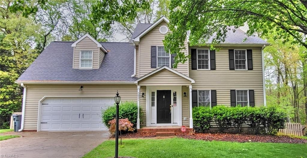 colonial home featuring roof with shingles, an attached garage, a front lawn, and concrete driveway