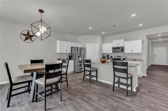 kitchen with light hardwood / wood-style floors, light stone counters, white cabinets, stainless steel appliances, and a center island