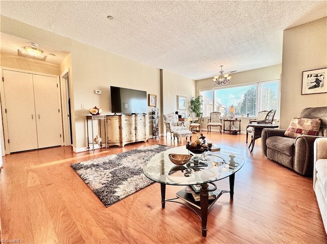 living room with light wood-type flooring, a textured ceiling, and a notable chandelier