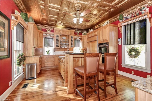 kitchen featuring crown molding, paneled built in fridge, stainless steel double oven, coffered ceiling, and light wood-type flooring