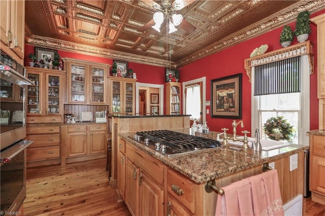 kitchen featuring ornamental molding, appliances with stainless steel finishes, a center island with sink, and light wood-type flooring