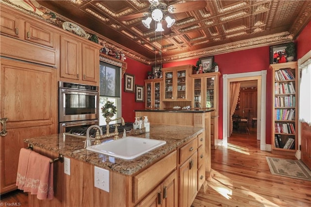 kitchen with hardwood / wood-style floors, sink, a center island with sink, and double oven