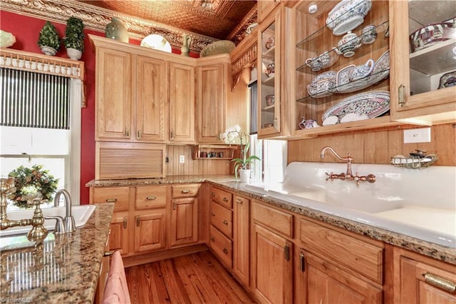 kitchen featuring wood-type flooring, light stone counters, sink, and a healthy amount of sunlight