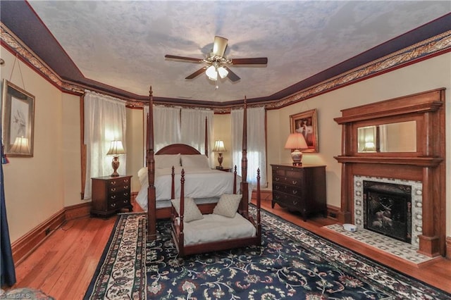 bedroom with crown molding, a tile fireplace, ceiling fan, and hardwood / wood-style floors