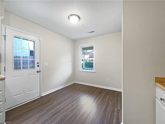 interior space with visible vents, dark wood finished floors, a textured ceiling, and baseboards