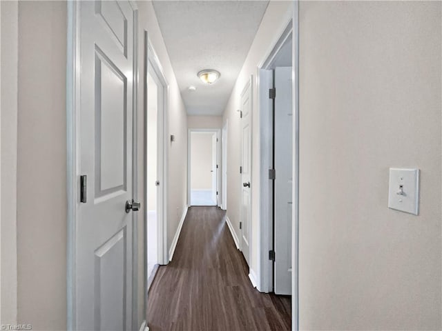 corridor featuring baseboards and dark wood-style flooring