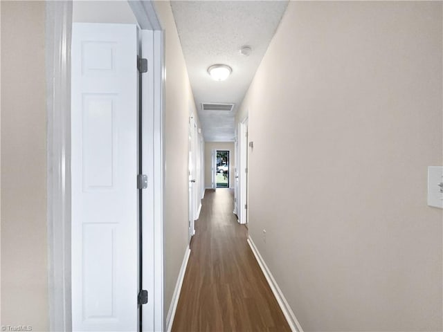 corridor featuring dark wood-style flooring, visible vents, a textured ceiling, and baseboards