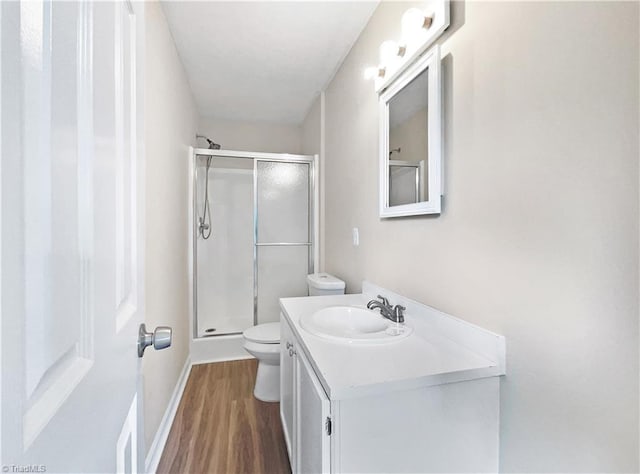 bathroom featuring baseboards, toilet, wood finished floors, vanity, and a shower stall