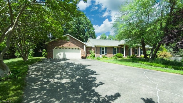 single story home with asphalt driveway, brick siding, a front yard, and a garage