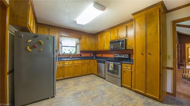 kitchen with stainless steel appliances, brown cabinetry, a sink, dark countertops, and a textured ceiling