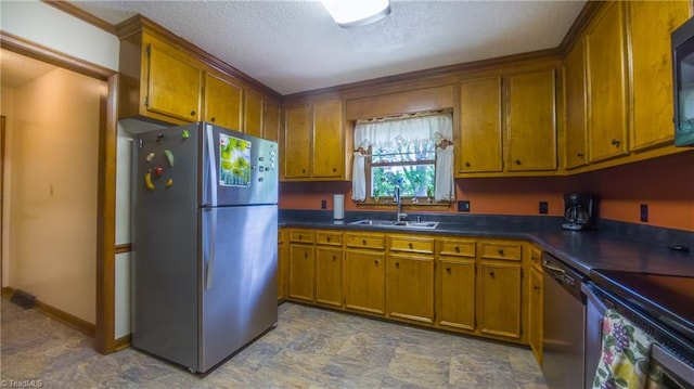 kitchen featuring stainless steel appliances, a sink, brown cabinetry, dark countertops, and a textured ceiling