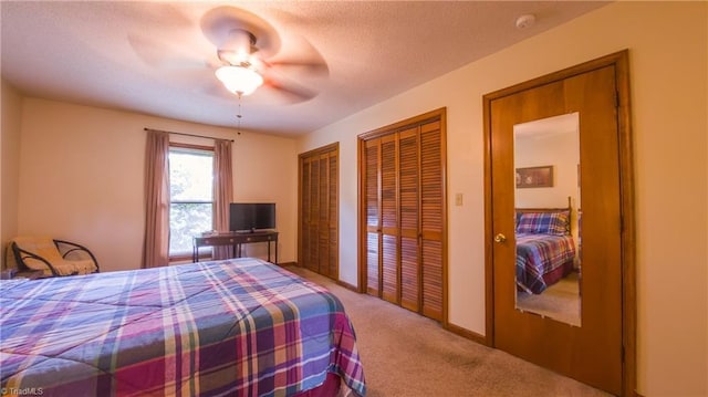 carpeted bedroom featuring two closets, ceiling fan, baseboards, and a textured ceiling