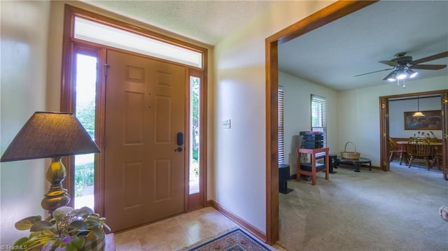 foyer featuring baseboards, ceiling fan, and light colored carpet