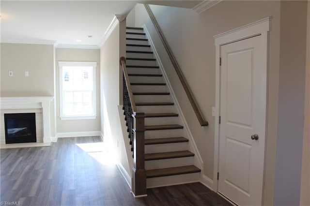 stairway with ornamental molding, a glass covered fireplace, baseboards, and wood finished floors