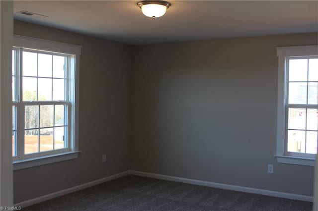 spare room with a healthy amount of sunlight, baseboards, and dark carpet