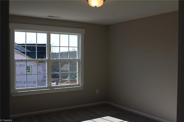 spare room featuring visible vents, baseboards, and dark colored carpet