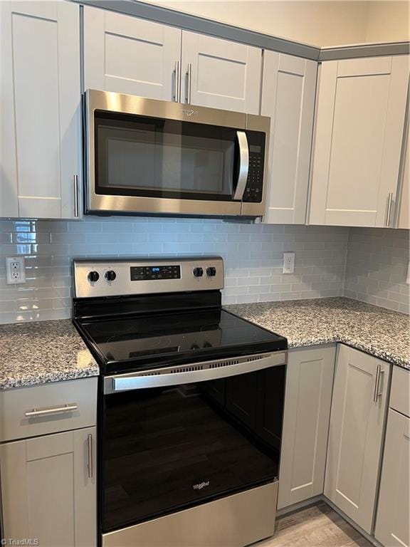 kitchen featuring white cabinets, decorative backsplash, light stone countertops, and appliances with stainless steel finishes