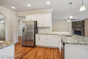 2834 Fallin Ct, High Point, NC 27262 - kitchen with stainless steel appliances, a ceiling fan, white cabinets, a peninsula, and a fireplace