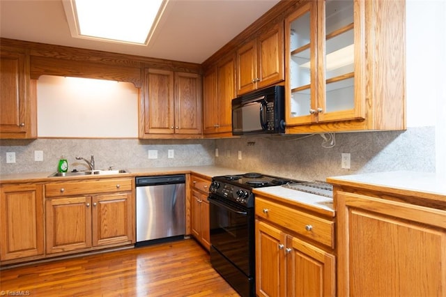 kitchen with black appliances, tasteful backsplash, light hardwood / wood-style floors, and sink