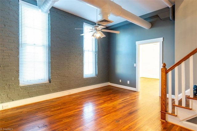 unfurnished room featuring brick wall, ceiling fan, and hardwood / wood-style floors