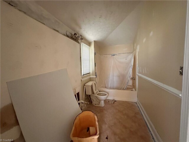 bathroom featuring shower / bathtub combination with curtain, toilet, baseboards, tile patterned flooring, and lofted ceiling