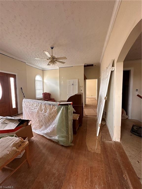 interior space with arched walkways, a textured ceiling, ornamental molding, and hardwood / wood-style flooring