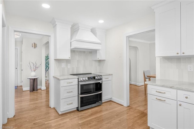 kitchen featuring range with two ovens, premium range hood, tasteful backsplash, baseboards, and arched walkways