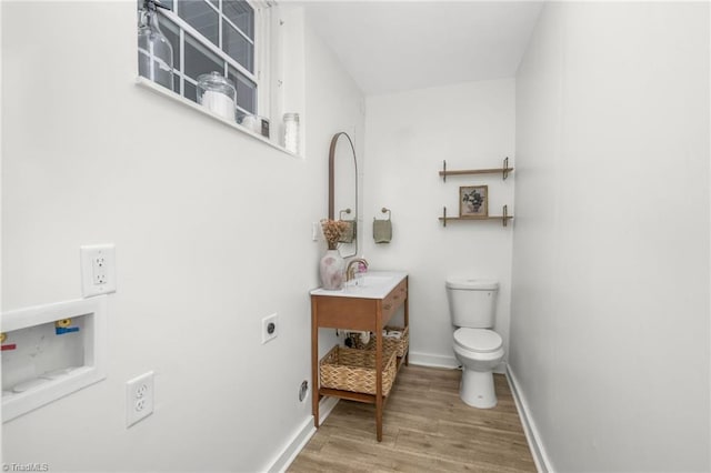 half bath with toilet, vanity, wood finished floors, and baseboards
