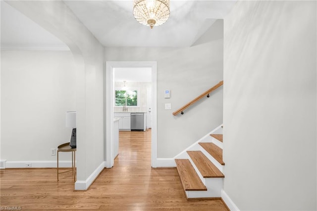 foyer entrance featuring wood finished floors, stairs, baseboards, arched walkways, and a chandelier