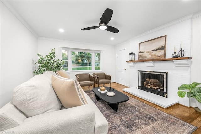 living room with wood finished floors, crown molding, a fireplace, ceiling fan, and recessed lighting