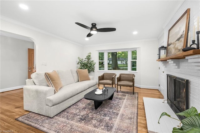 living area with ceiling fan, light wood-style floors, a brick fireplace, baseboards, and crown molding