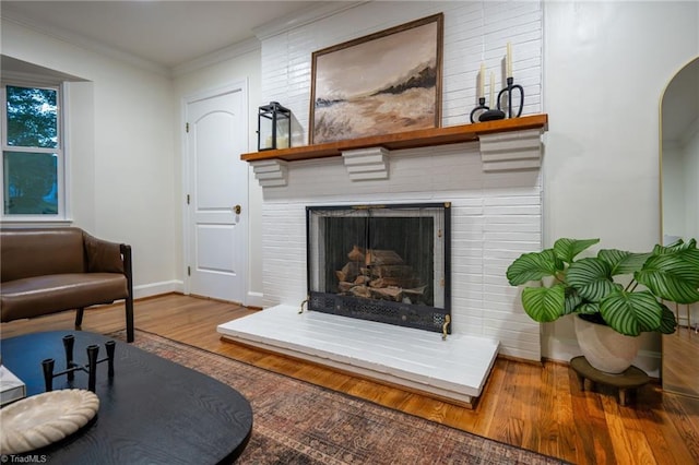 living room featuring wood finished floors, baseboards, a fireplace, crown molding, and arched walkways