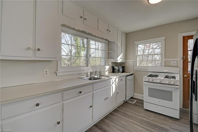 kitchen with sink, white appliances, white cabinets, and hardwood / wood-style flooring