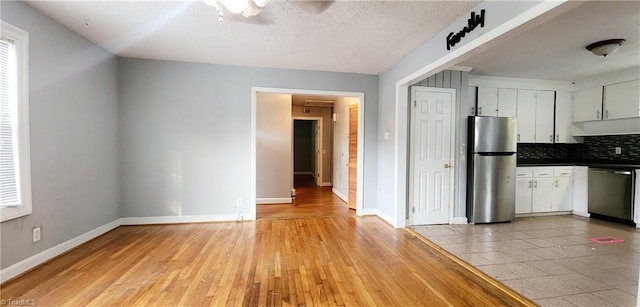 kitchen featuring white cabinets, appliances with stainless steel finishes, decorative backsplash, and light hardwood / wood-style flooring