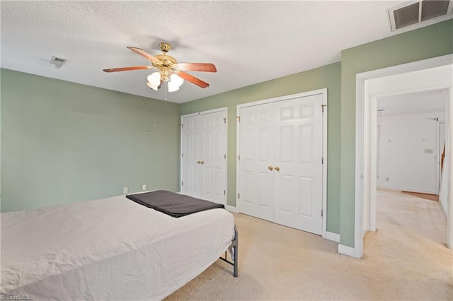 carpeted bedroom featuring a textured ceiling, two closets, and ceiling fan