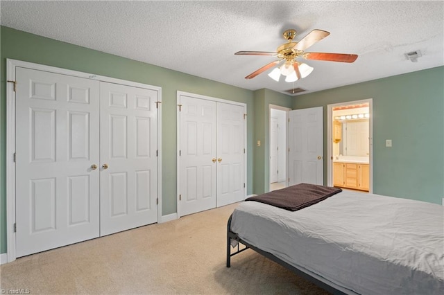 bedroom featuring connected bathroom, multiple closets, ceiling fan, a textured ceiling, and light carpet