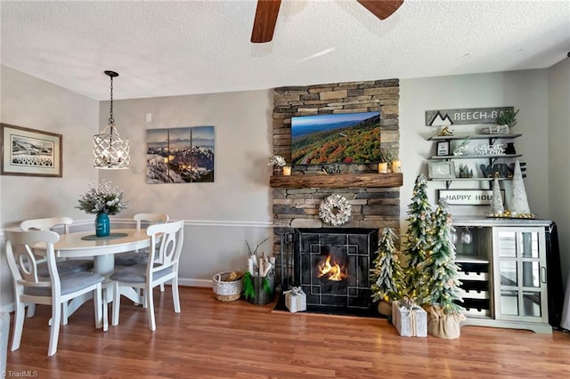 dining room featuring ceiling fan, a fireplace, hardwood / wood-style floors, and a textured ceiling