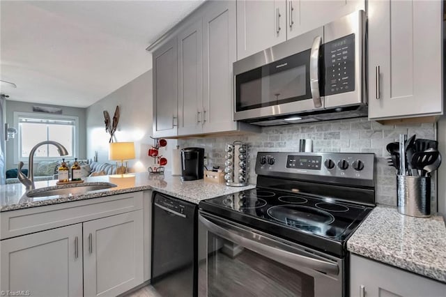 kitchen featuring backsplash, light stone counters, gray cabinetry, stainless steel appliances, and sink