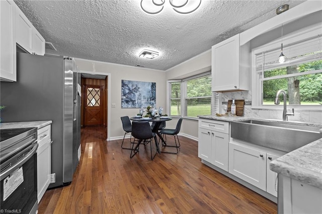 kitchen with white cabinetry, sink, hanging light fixtures, backsplash, and range