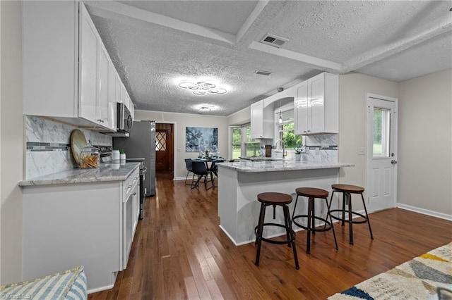 kitchen featuring tasteful backsplash, dark hardwood / wood-style floors, kitchen peninsula, a breakfast bar, and white cabinets