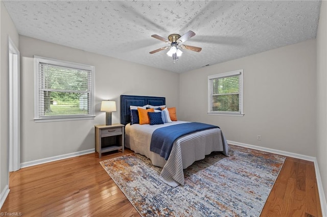 bedroom featuring multiple windows, ceiling fan, hardwood / wood-style floors, and a textured ceiling