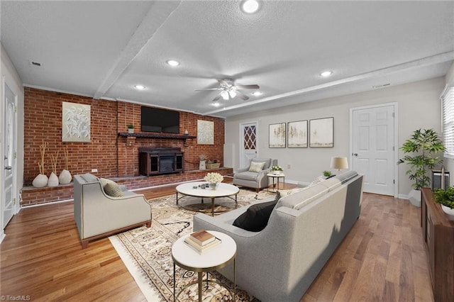 living room featuring ceiling fan, beamed ceiling, brick wall, a textured ceiling, and hardwood / wood-style flooring