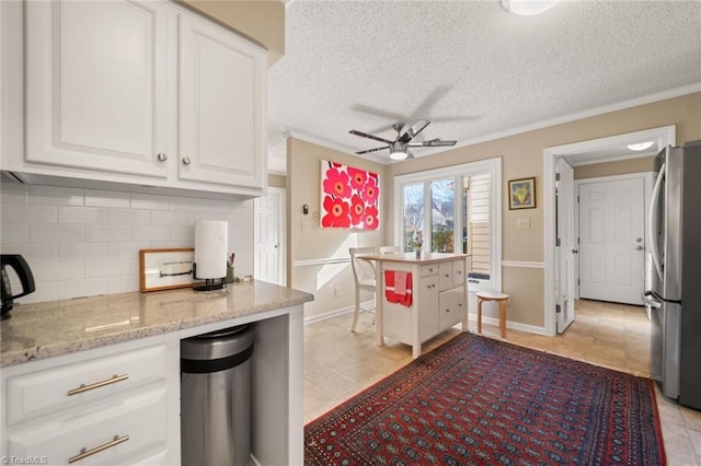 kitchen with tasteful backsplash, light stone counters, stainless steel refrigerator, ceiling fan, and white cabinets