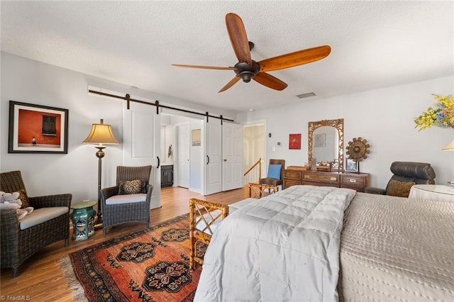 bedroom featuring ceiling fan, a barn door, a textured ceiling, and light wood-type flooring